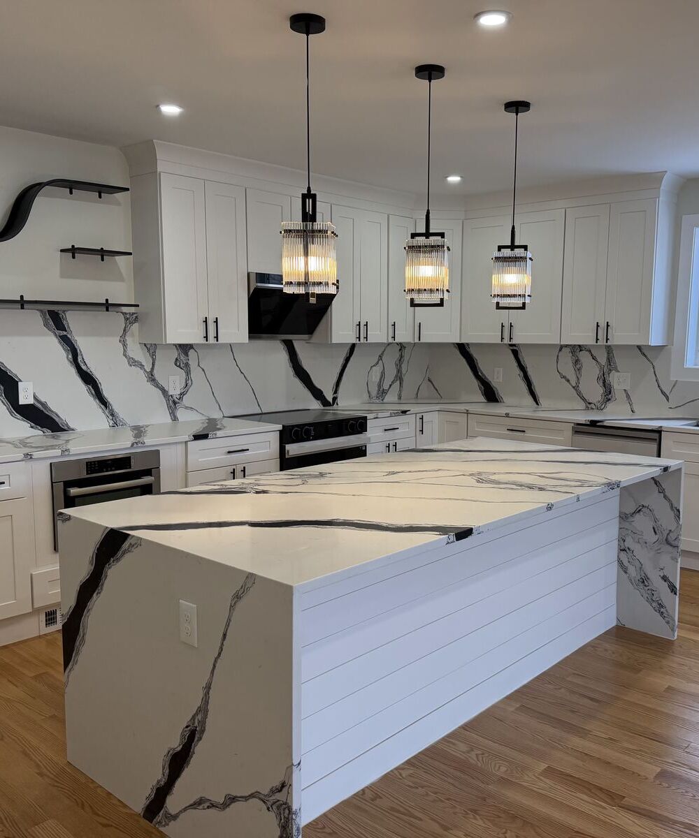 Remodeled kitchen with white shaker cabinets, waterfall quartz island with black veining and glass pendant lights